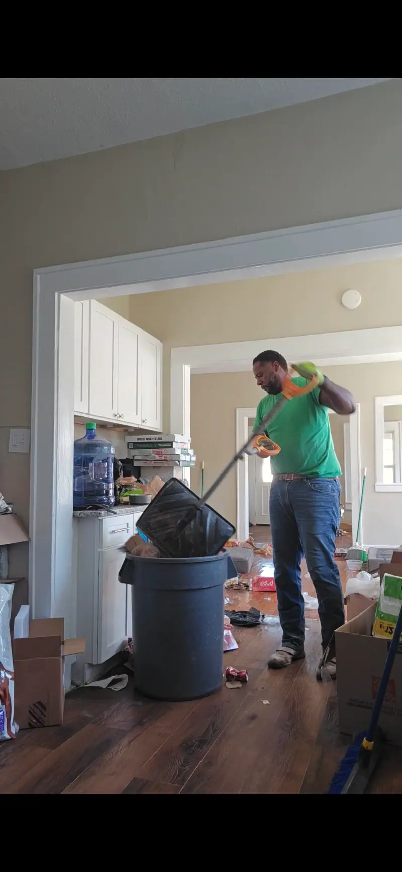 A Racoons crew member in a green shirt bagging trash during a house cleanout