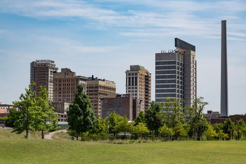 Downtown Birmingham high-rises and a tall smokestack seen across the lawn of Railroad Park